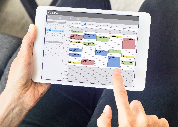 Calendar app on tablet computer with planning of the week with appointments, events, tasks, and meeting. Hands holding device, time management concept, organization of working hours planner, schedule