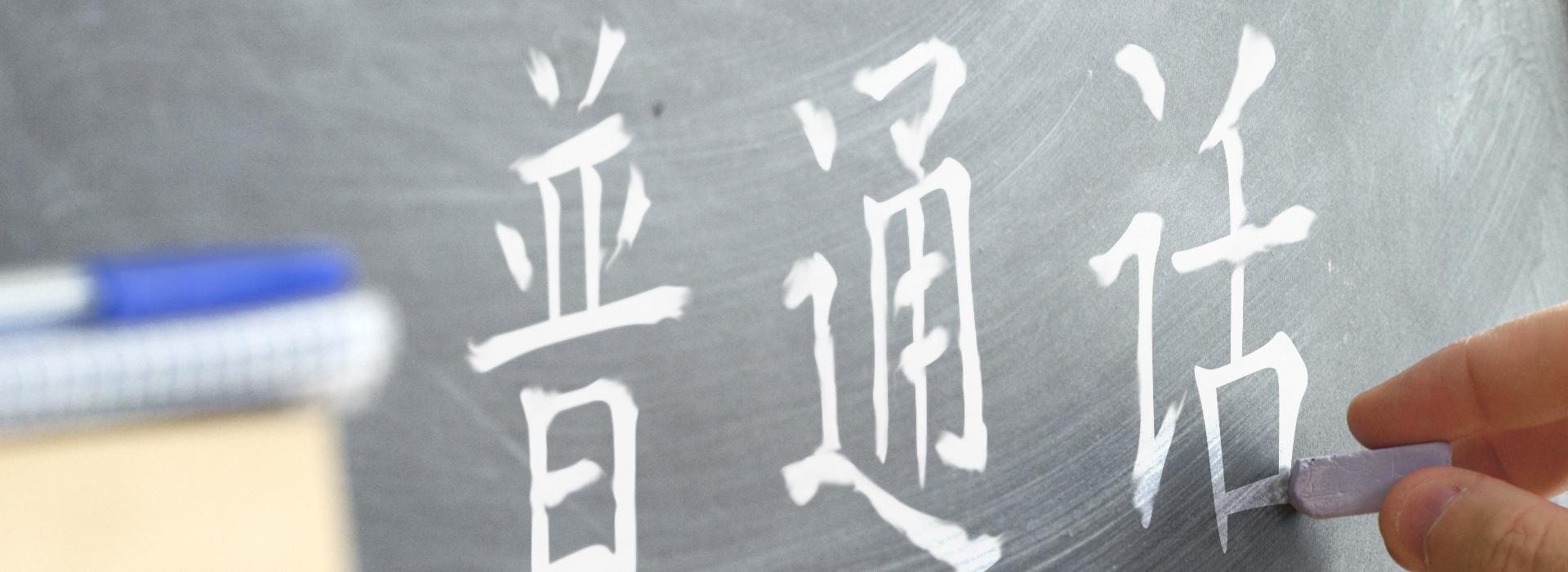 Hand writing on a blackboard in a Chinese class. Some books and school materials.