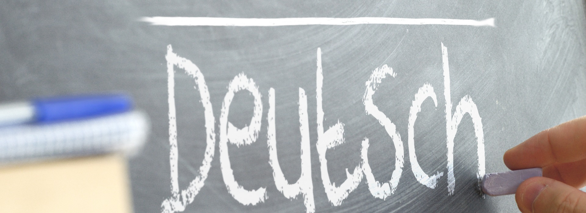 Hand writing on a blackboard in a language class with the word "German" wrote on. Some books and school materials.