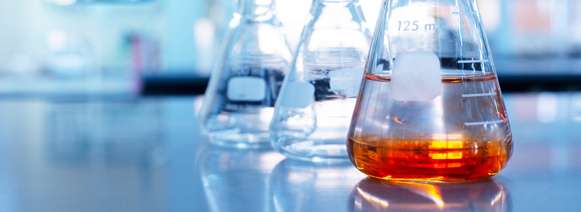 orange solution in science glass flask in blue chemistry school laboratory background