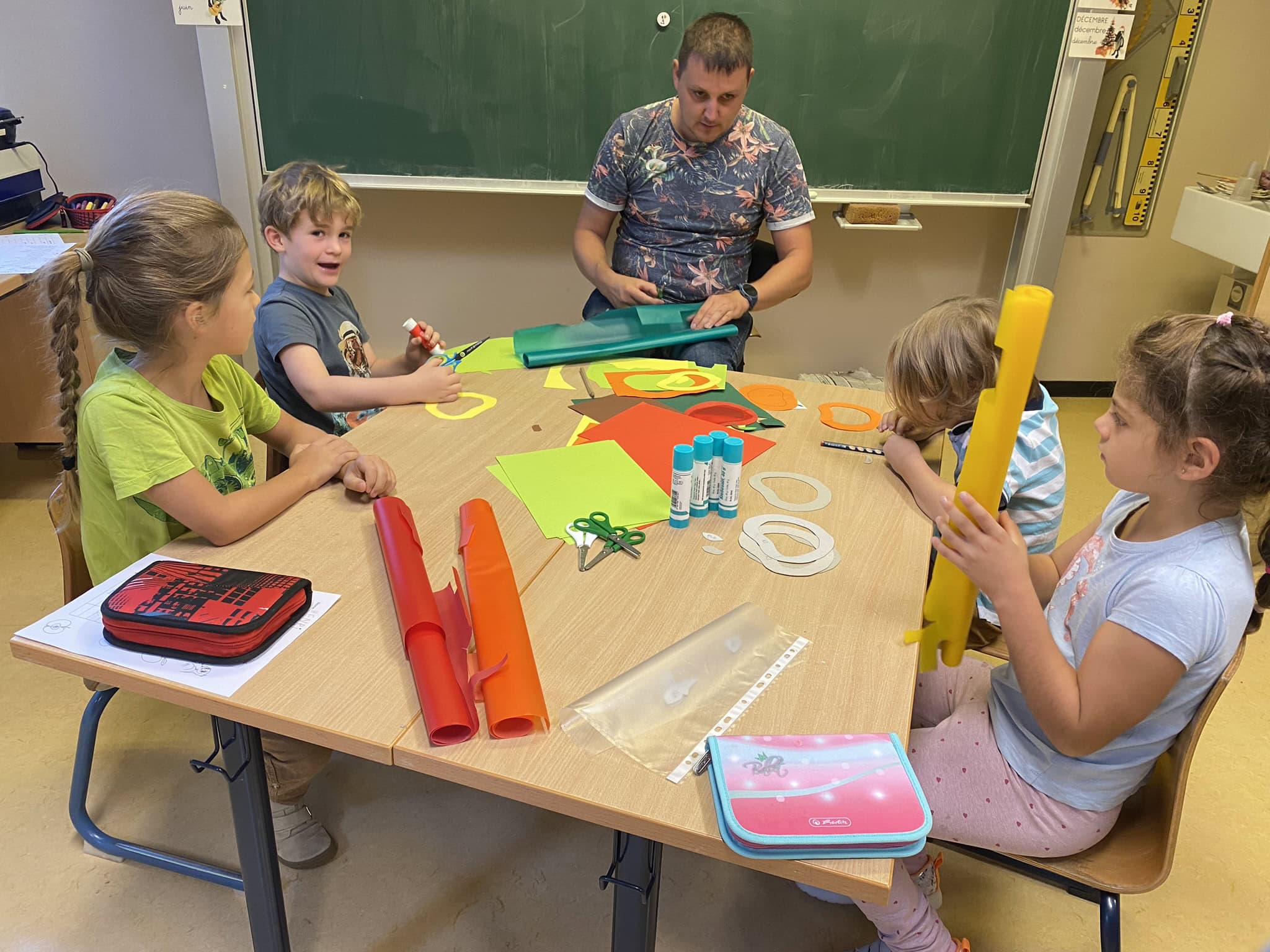 Eine Gruppe von Kindern und ein Betreuer basteln bunte Papierkunstwerke an einem Tisch.