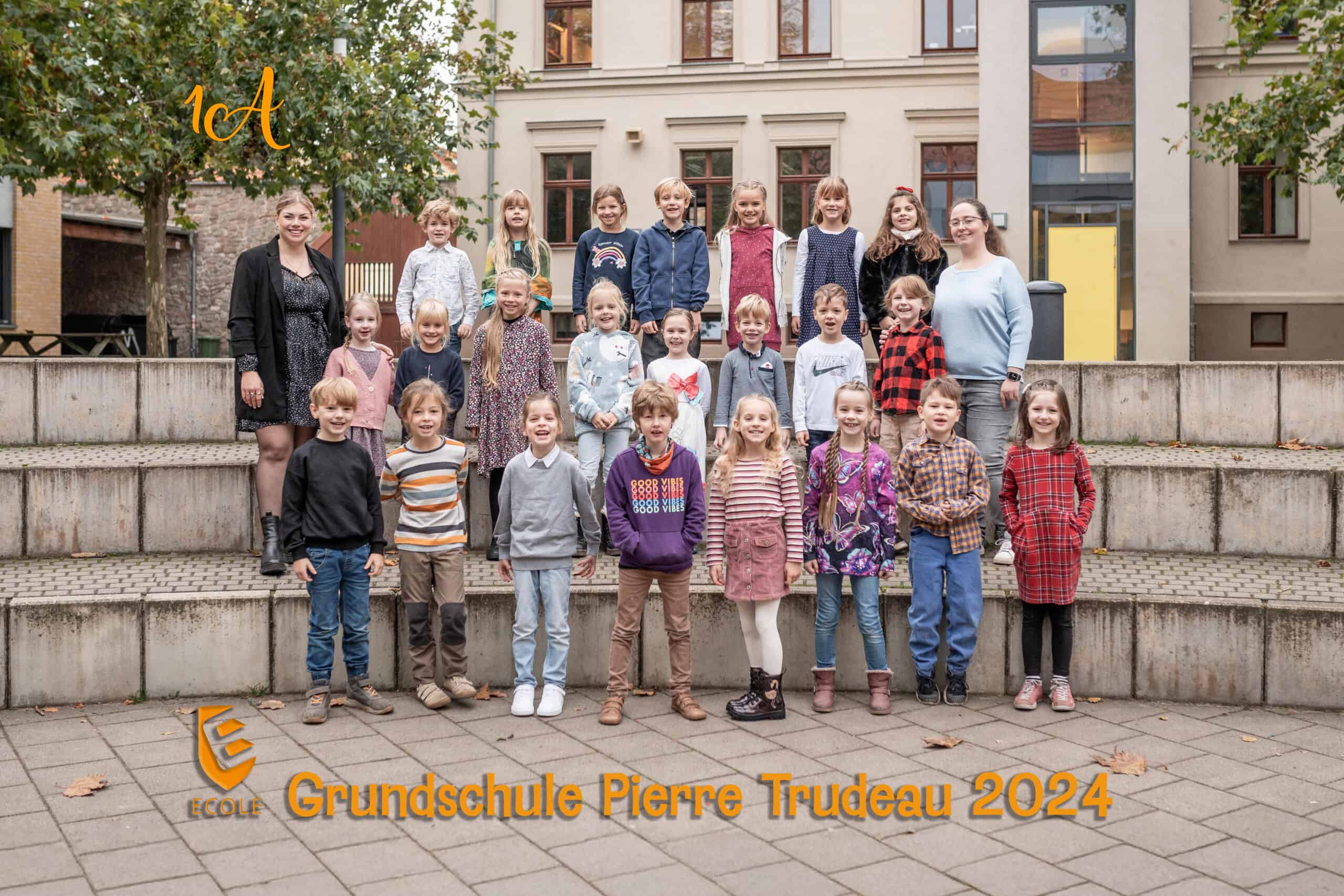 Kindergruppe und zwei Erwachsene lachen; Herbstfarben, Schulhof im Hintergrund.