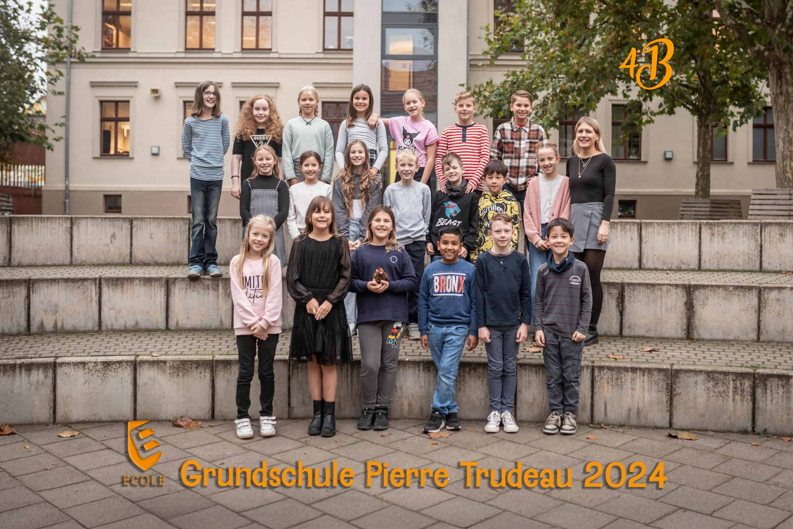 Kindergruppe vor Schulgebäude, freundlich lächelnd, Herbstfarben, Lehrerin rechts stehend.
