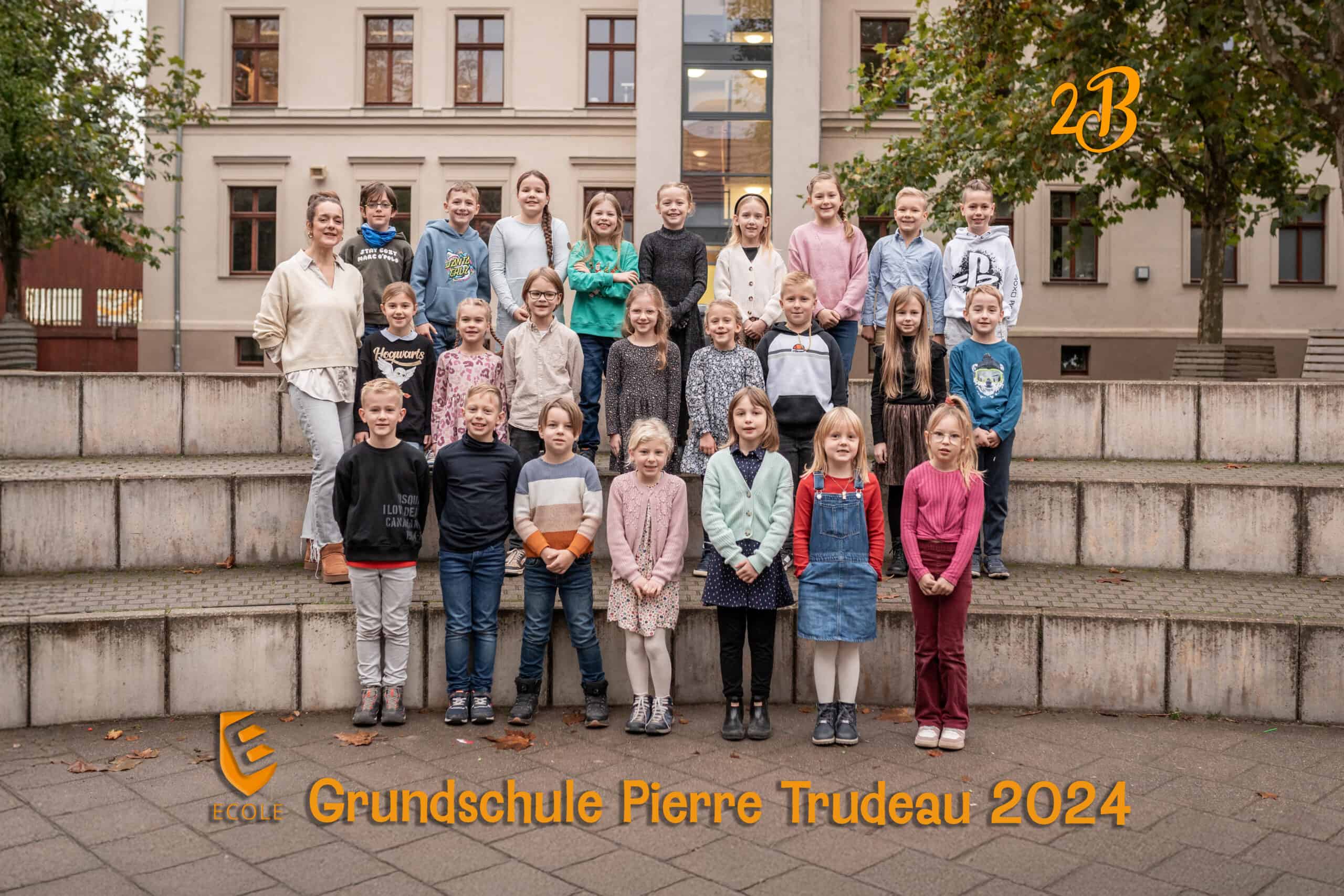 Eine Gruppe von 25 fröhlichen Kindern und einer Lehrerin, vor einer Schulgebäude-Kulisse.