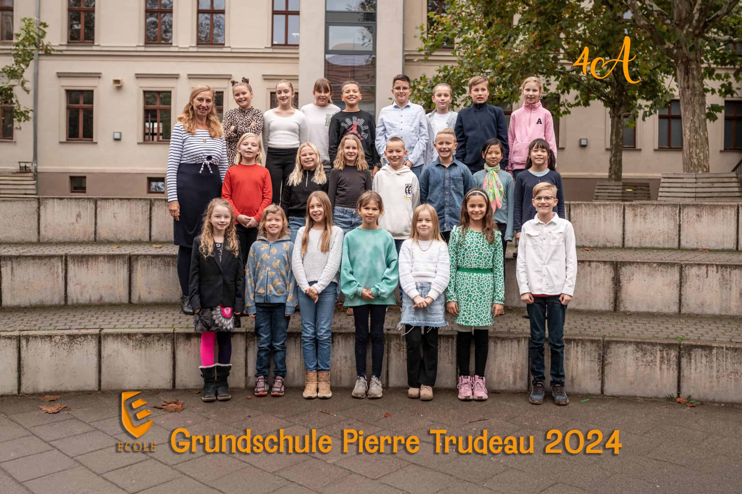 Eine Gruppe von Schülern mit Lehrerin, lächelnd, draußen vor einem Schulgebäude.