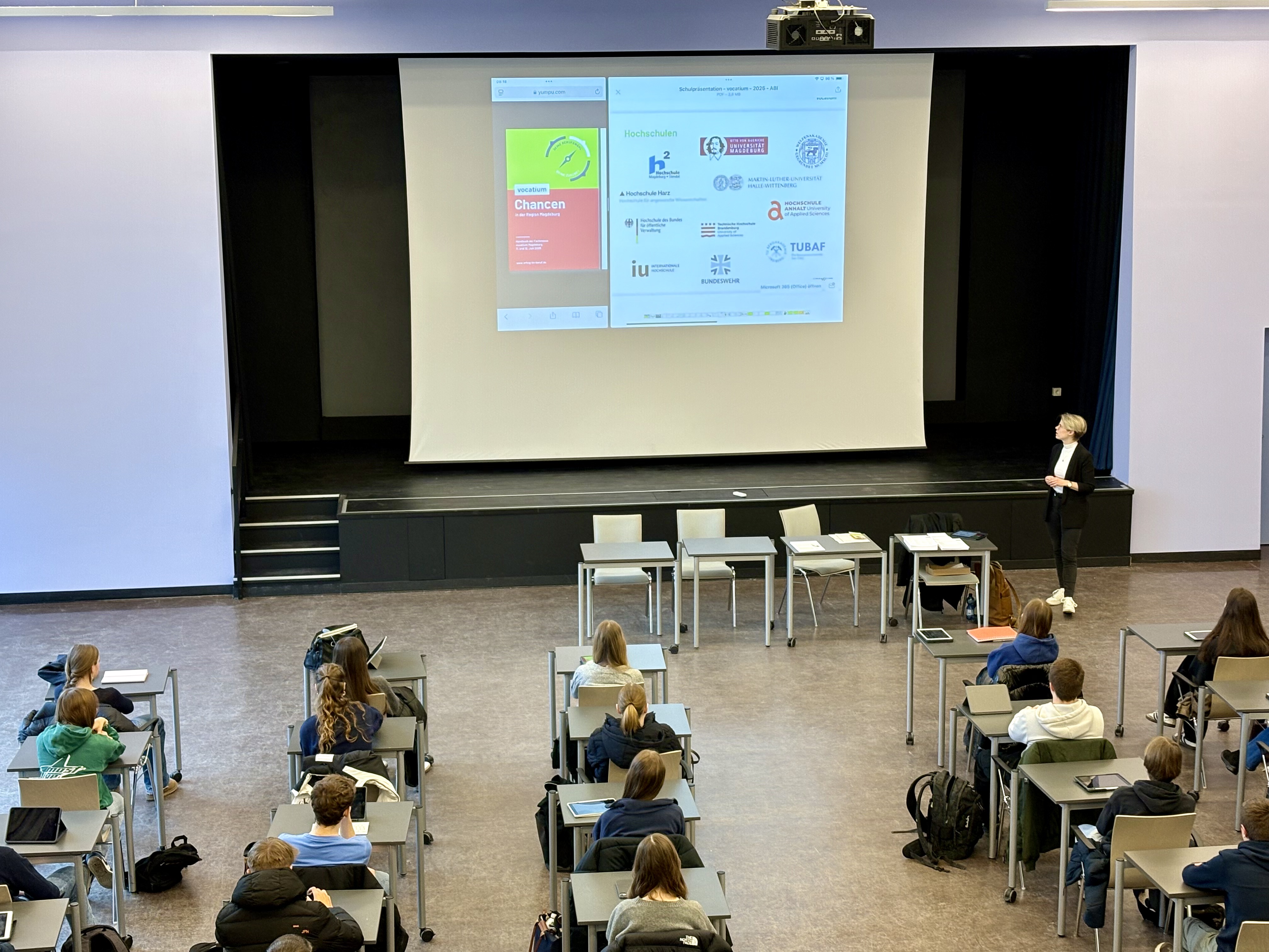 Eine Gruppe Studierender sitzt in einem Hörsaal, während eine Person vorne etwas präsentiert.