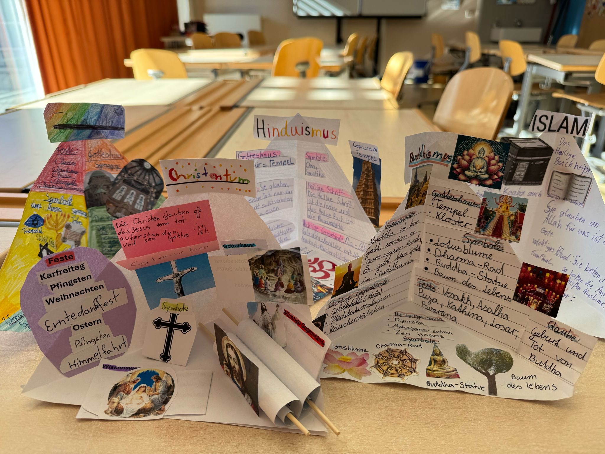 Farbig gestaltete Präsentation über Religionen mit diversen Bildern und Texten auf Tisch in Klassenzimmer.