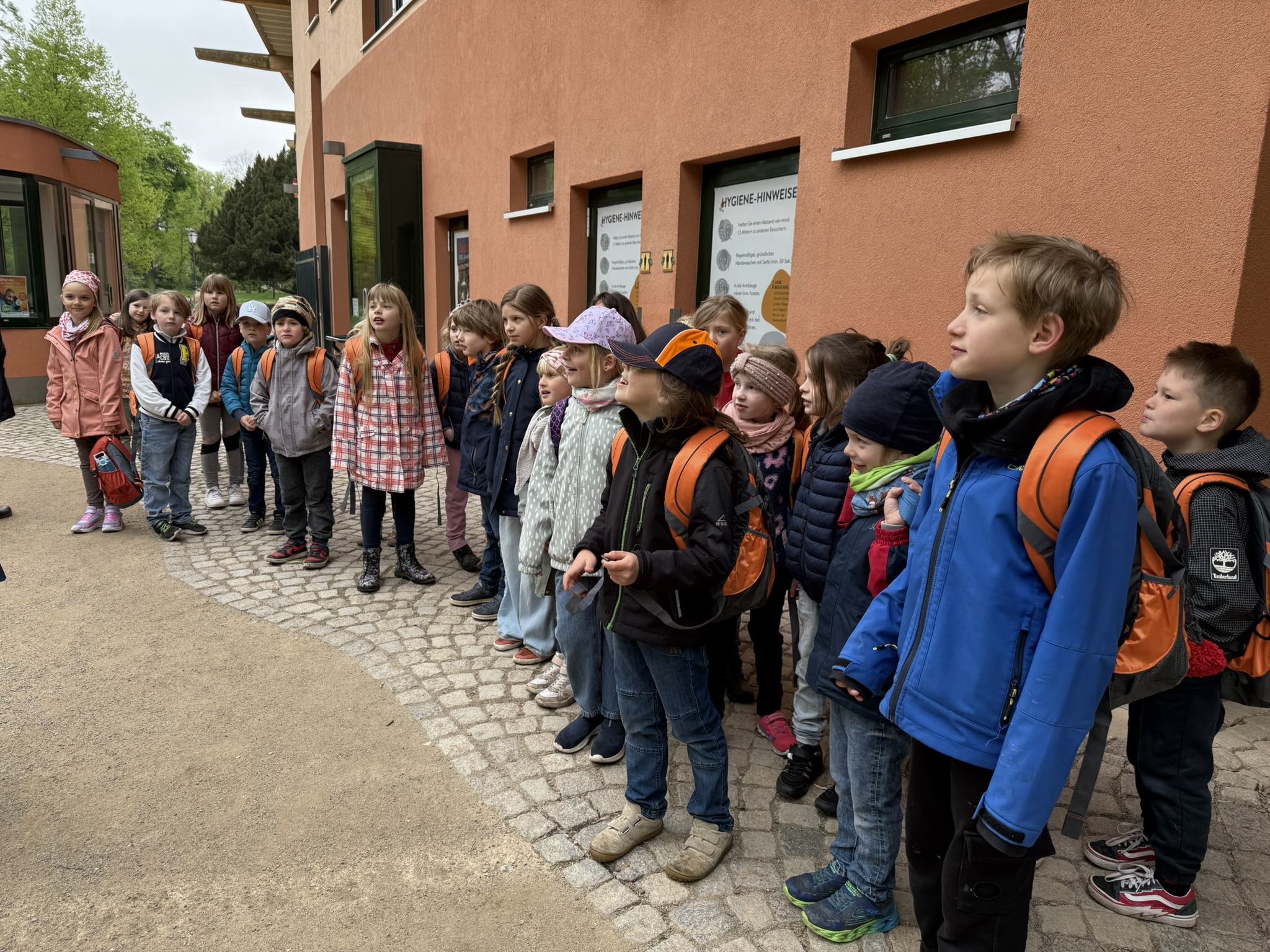 Eine Gruppe von Kindern in bunter Kleidung steht auf einem Gehweg und blickt nach rechts.