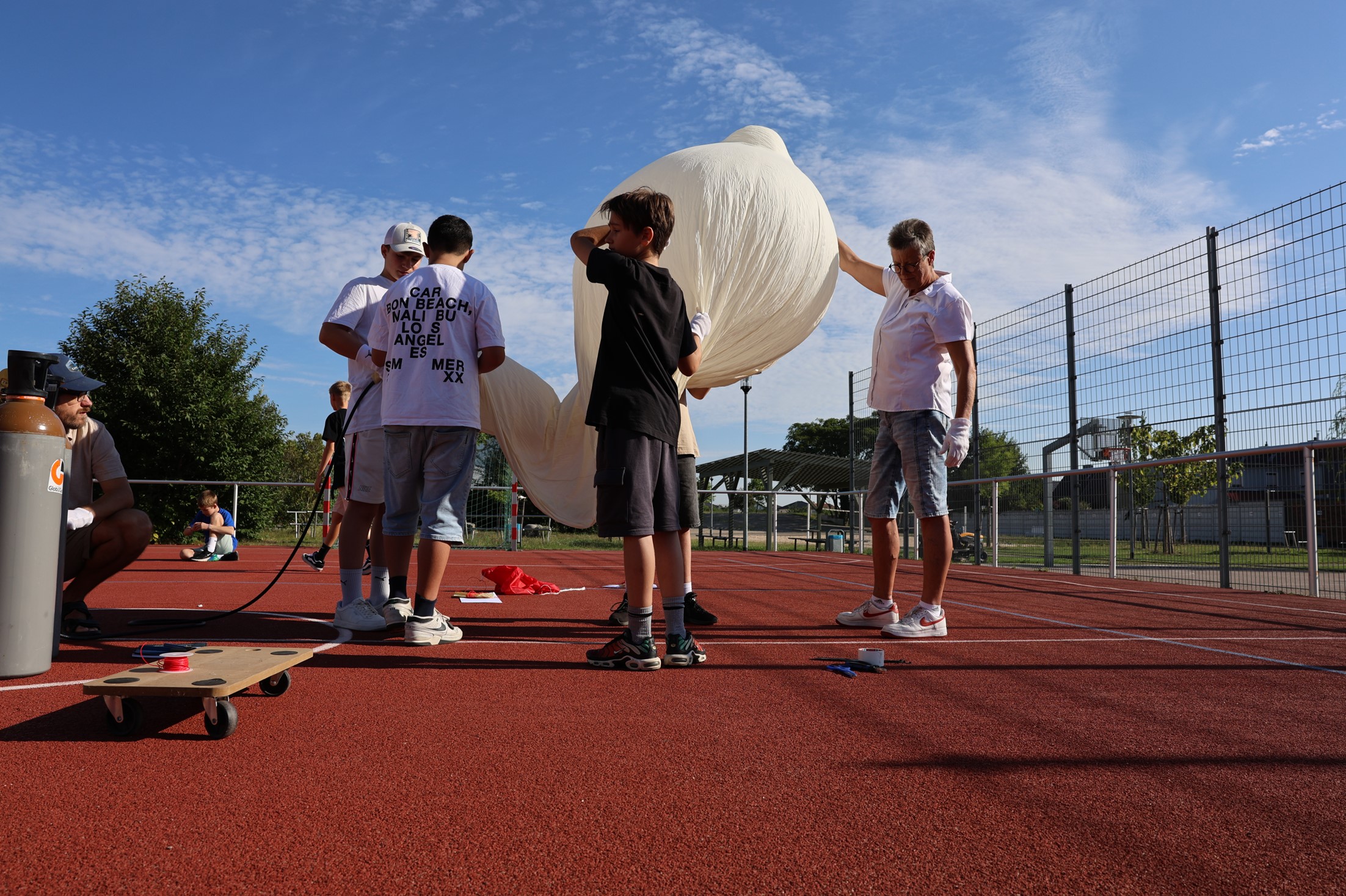 Gruppe von Personen auf Sportplatz hält großen weißen Ballon mit konzentriertem Ausdruck.