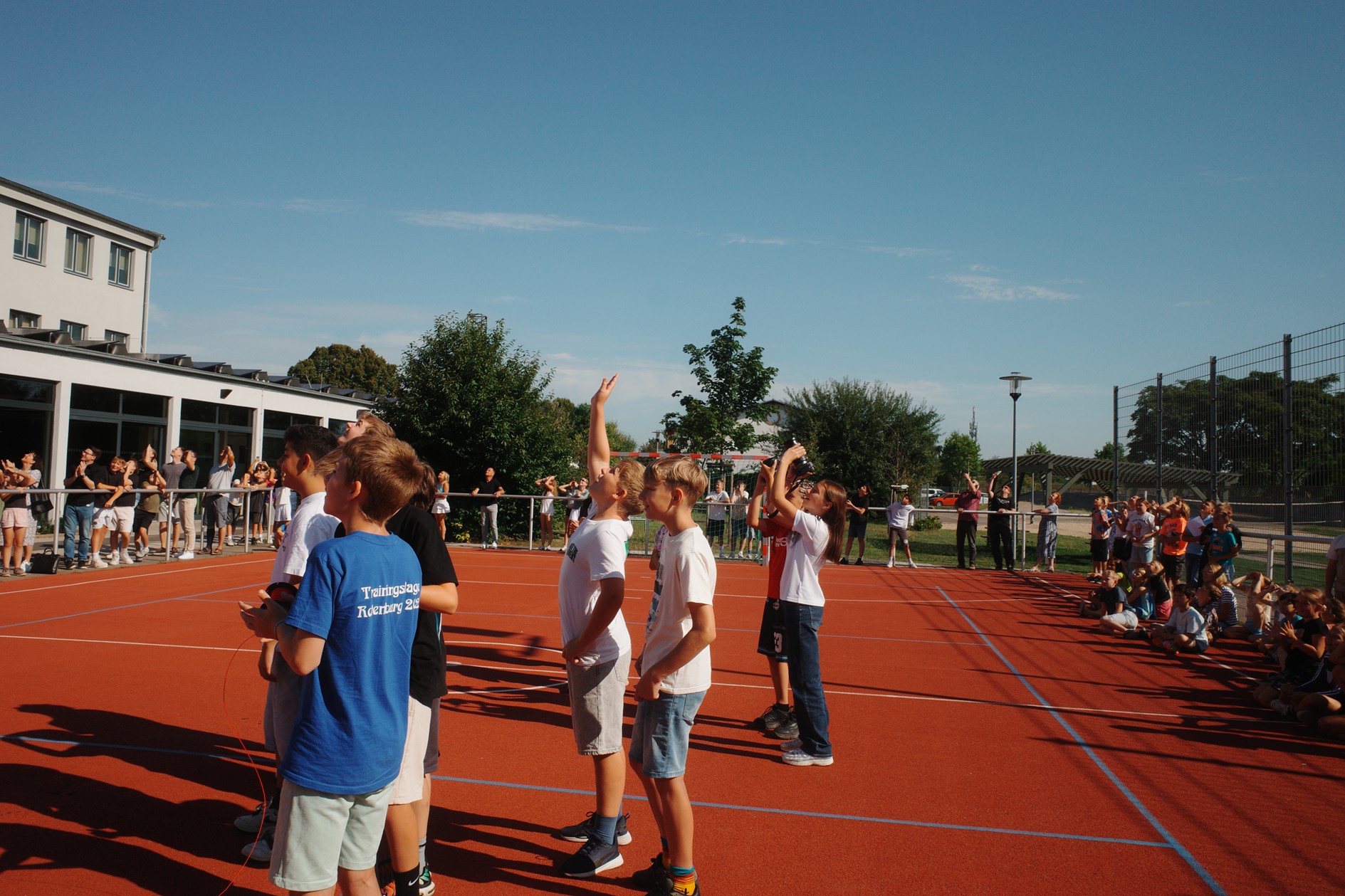 Mehrere Jugendliche auf einem Sportplatz tragen helle Kleidung und schauen nach oben
