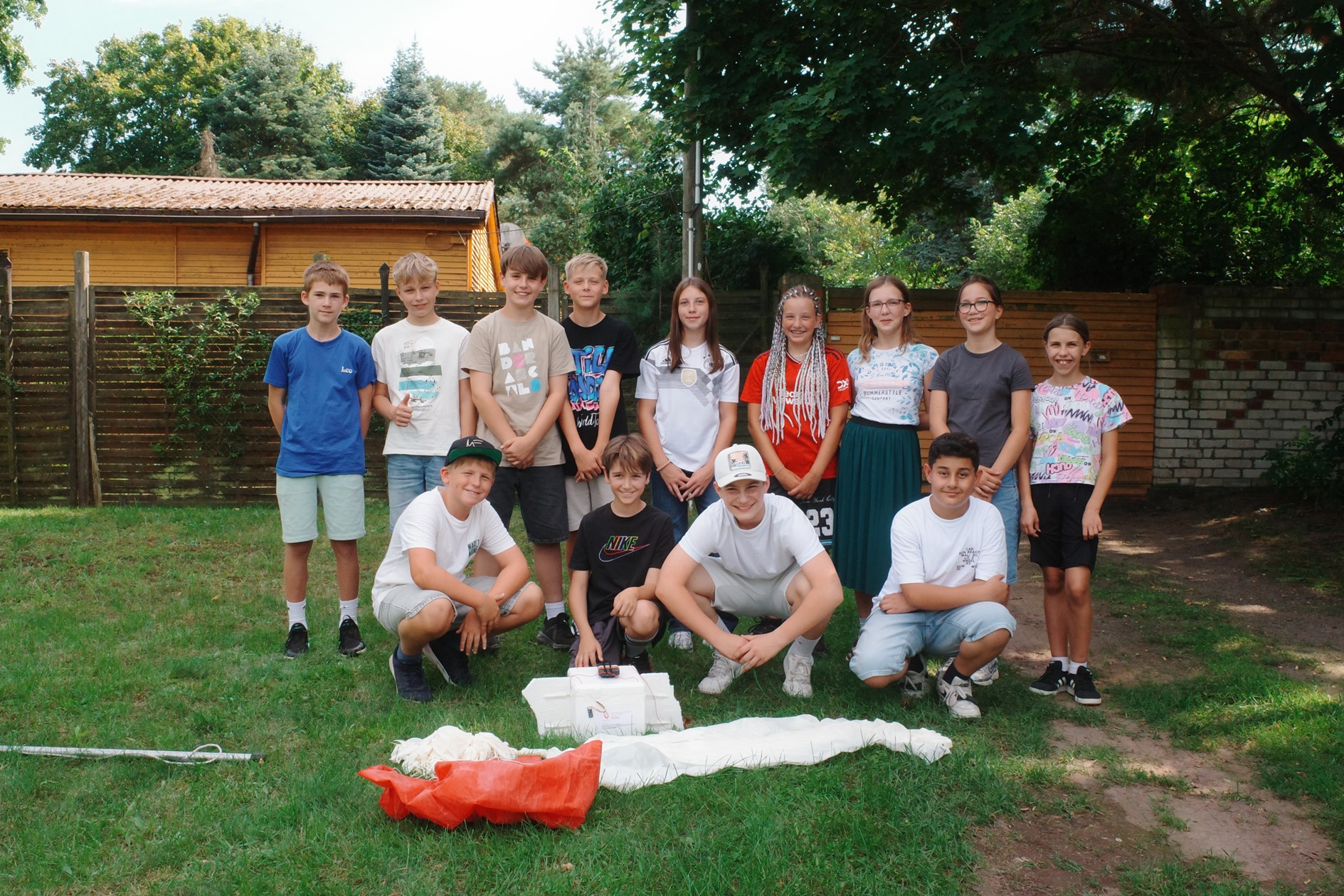 Eine Gruppe Jugendlicher lächelt im Freien vor einer Holzhütte.