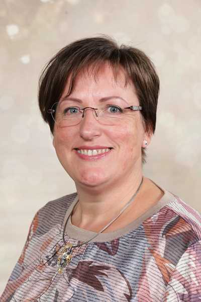 Eine lächelnde Frau mit Brille, kurzem braunem Haar und gemustertem Oberteil.