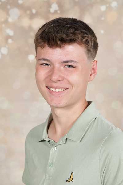 Ein lächelnder junger Mann mit kurzem braunem Haar trägt ein grünes Polohemd.