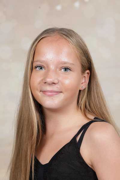 Junge Frau mit langem blondem Haar lächelt, trägt ein schwarzes Oberteil.