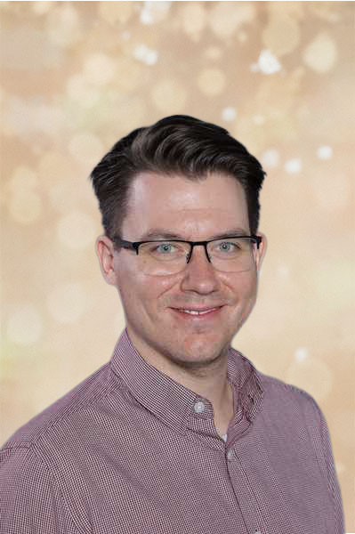 Ein lächelnder Mann mit Brille in einem karierten Hemd vor einem verschwommenen Hintergrund