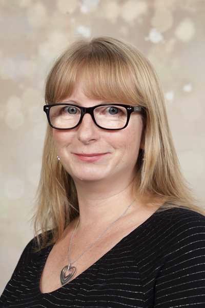 Eine Frau mit Brille lächelt leicht, trägt ein schwarzes Top und hat blondes Haar.