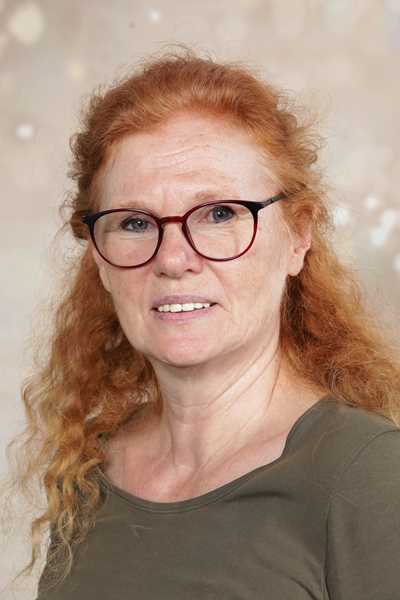 Frau mit lockigem rotem Haar und Brille lächelt leicht vor neutralem Hintergrund