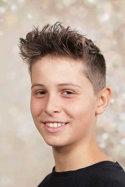 Ein lächelnder Junge mit kurzem, braunem Haar vor neutralem Hintergrund