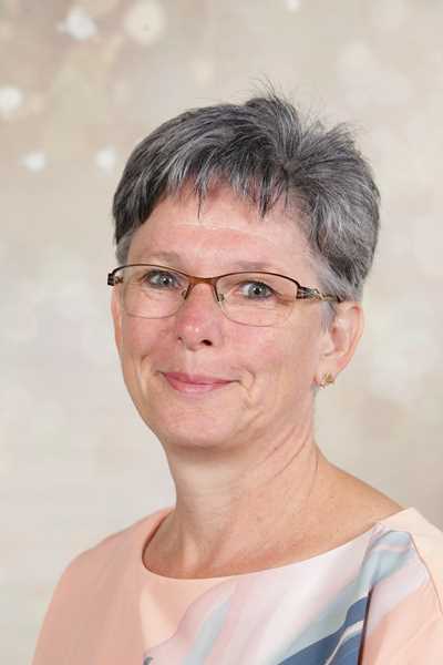 Eine freundliche ältere Frau mit grauem Haar und Brille lächelt sanft.