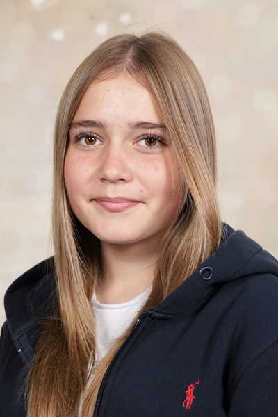 Eine junge Frau mit langen blonden Haaren lächelt dezent in die Kamera, bekleidet mit einem dunkelblauen Kapuzenpullover.
