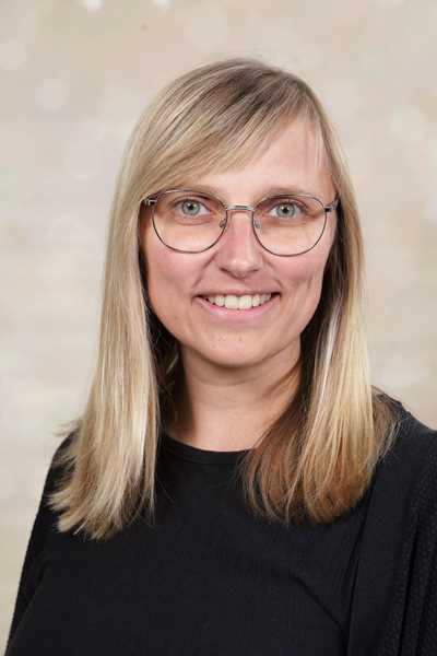 Eine lächelnde Frau mit langen blonden Haaren und Brille in schwarzer Kleidung