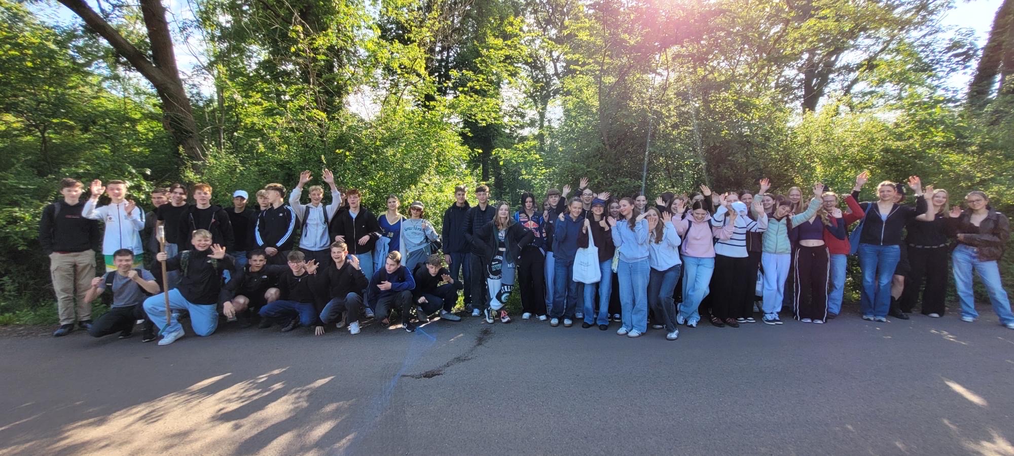 Eine große Gruppe von Menschen steht draußen auf einer Straße und winkt fröhlich.