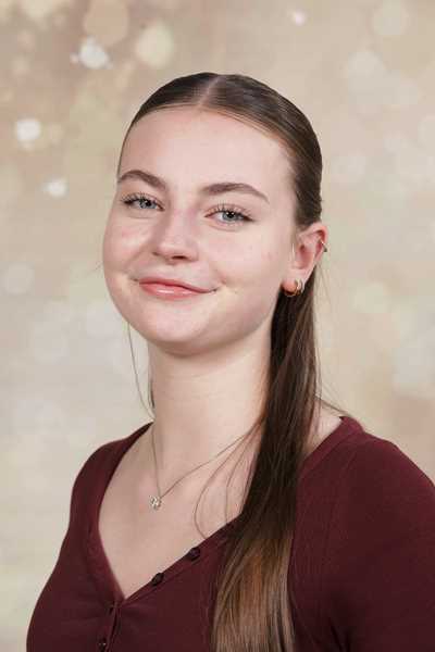 Eine lächelnde junge Frau mit langen braunen Haaren vor einem beigen Hintergrund