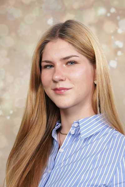 Eine lächelnde Frau mit langen blonden Haaren in einem blau-weiß gestreiften Hemd.