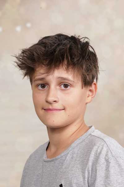 Junger Mann mit verwuschelten Haaren und neutralem Ausdruck in grauem T-Shirt.