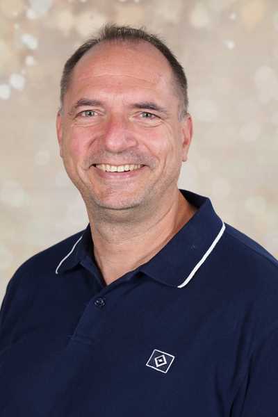Ein lächelnder Mann in einem blauen Poloshirt vor einem hellen Hintergrund.