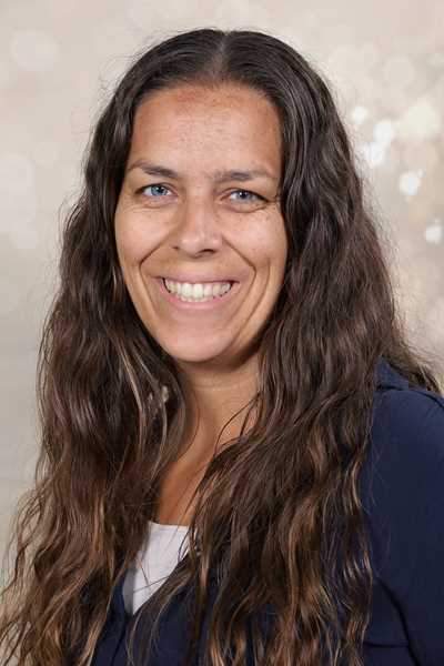 Eine lächelnde Frau mit langen, braunen Haaren und einem blauen Oberteil.