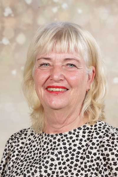 Eine ältere Frau mit blondem Haar lächelt freundlich, trägt ein gepunktetes Oberteil.