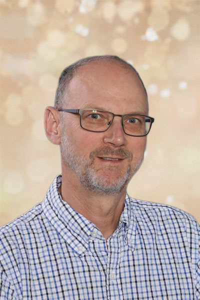 Ein lächelnder Mann mit Brille, grauem Bart und kariertem Hemd vor unscharfem Hintergrund