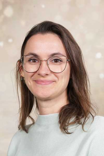 Eine lächelnde Frau mit Brille, braunen Haaren und hellem Pullover vor hellem Hintergrund