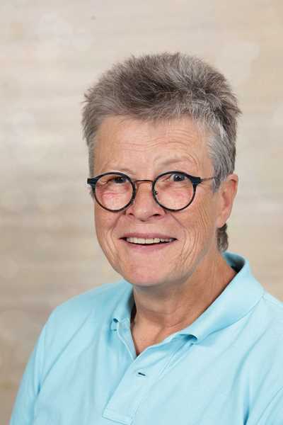 Eine lächelnde Person mit Brille und kurzen grauen Haaren trägt ein blaues Polohemd.