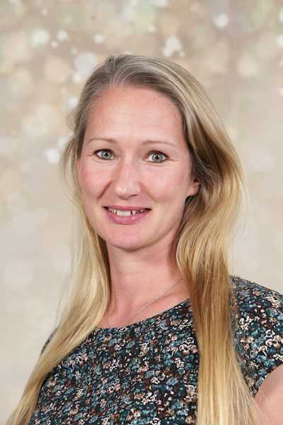Eine lächelnde Frau mit langen blonden Haaren, gemustertes Oberteil, helle Hintergründe