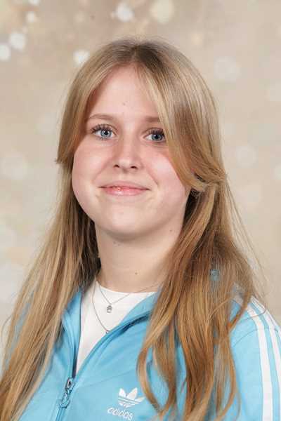 Eine junge Frau mit blonden Haaren lächelt sanft in einer blauen Jacke.