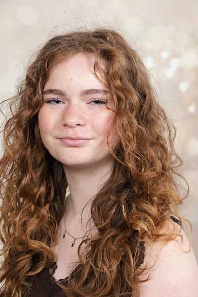 Eine junge Frau mit lockigem, rötlichem Haar lächelt leicht in die Kamera.
