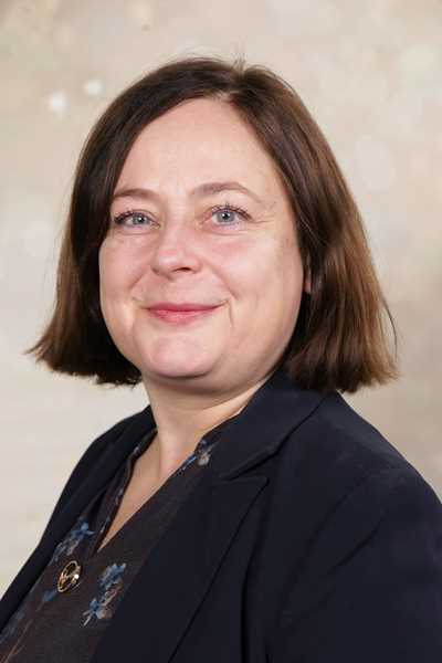 Eine lächelnde Frau mit schulterlangem braunem Haar und dunklem Blazer.