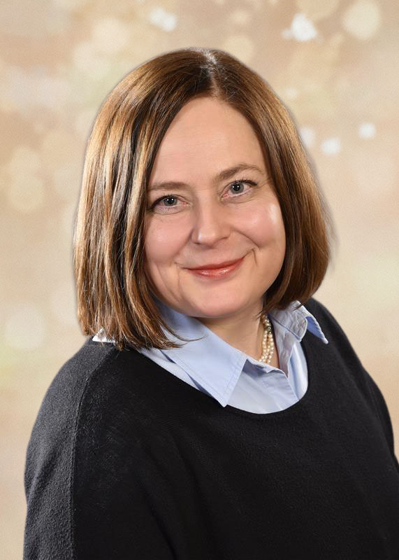 Eine lächelnde Frau mit glattem braunem Haar und einem schwarzen Pullover.