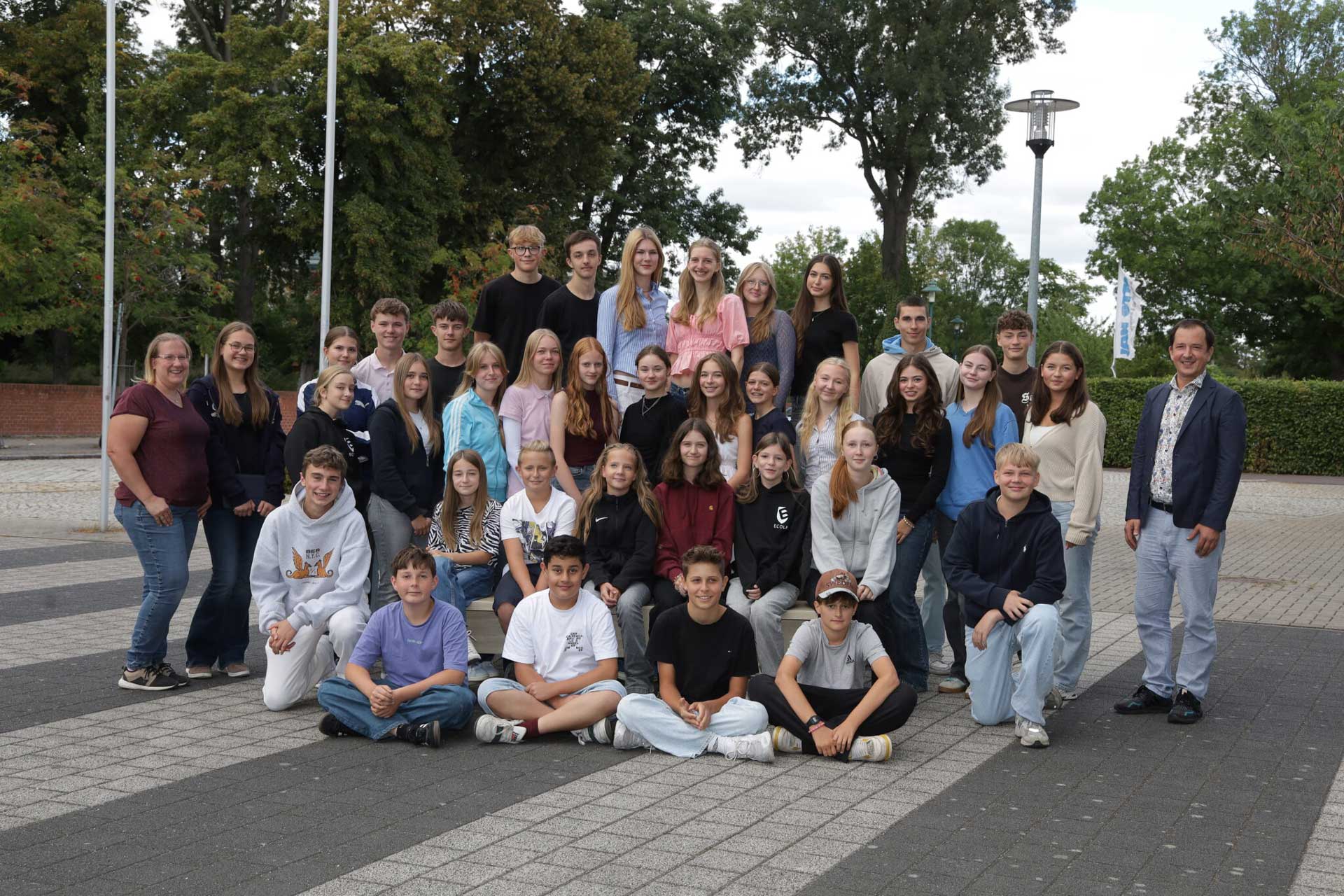 Eine Gruppe junger Menschen posiert fröhlich draußen in bunter Freizeitkleidung.