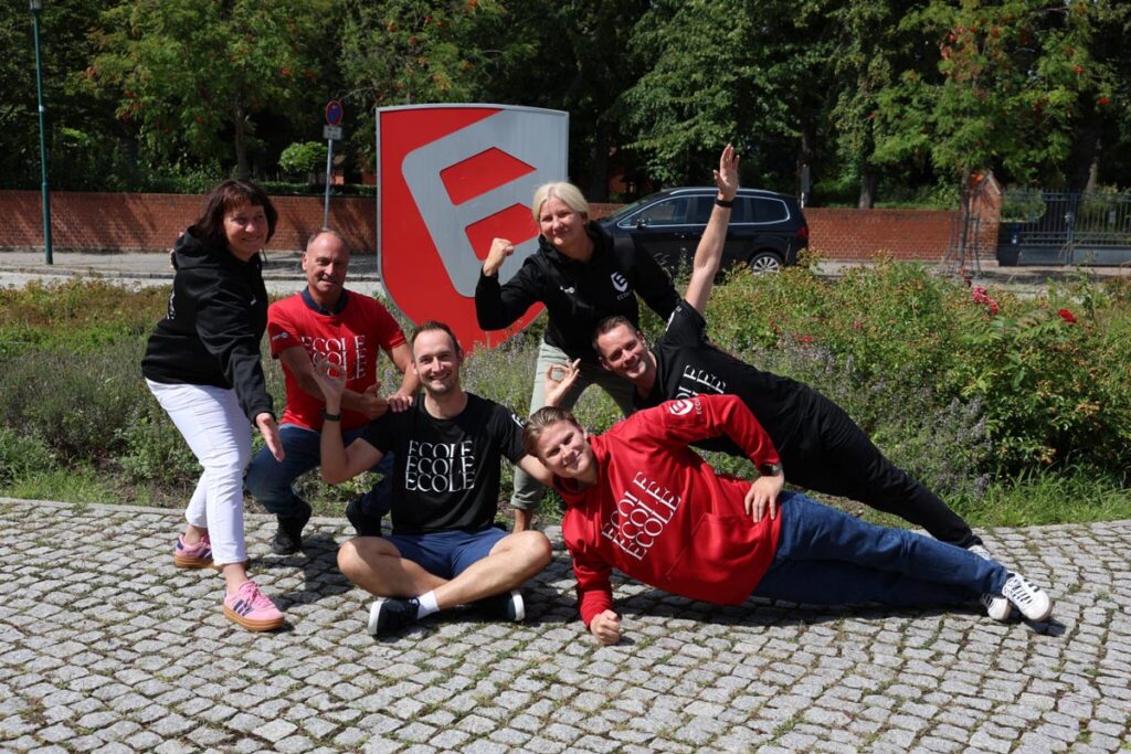 Eine Gruppe von sechs Personen posiert lächelnd auf einem gepflasterten Weg.