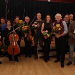 Gruppe von Personen mit Musikinstrumenten und Blumen, lächeln freundlich.