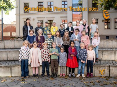 Eine Gruppe fröhlicher Grundschulkinder mit ihrer Lehrerin posiert vor der Schule