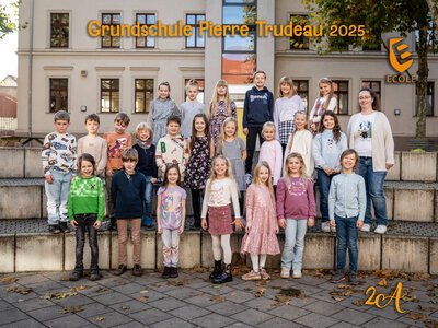 Eine Gruppe von Grundschulkindern und einer Lehrerin lächeln auf einer Treppe draußen