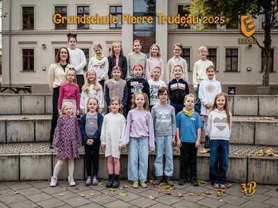 Eine fröhliche Grundschulklasse mit ihrer Lehrerin posiert vor einer Schule draußen