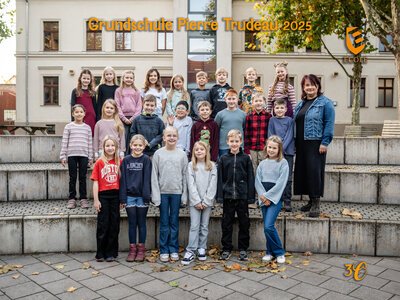 Eine fröhliche Kindergruppe mit ihrer Lehrerin steht draußen vor einer Schule