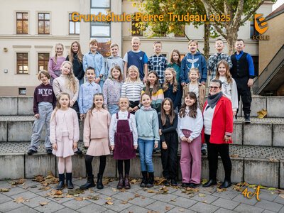 Eine Gruppe lächelnder Schulkinder und eine Erwachsene posieren draußen vor einer Schule