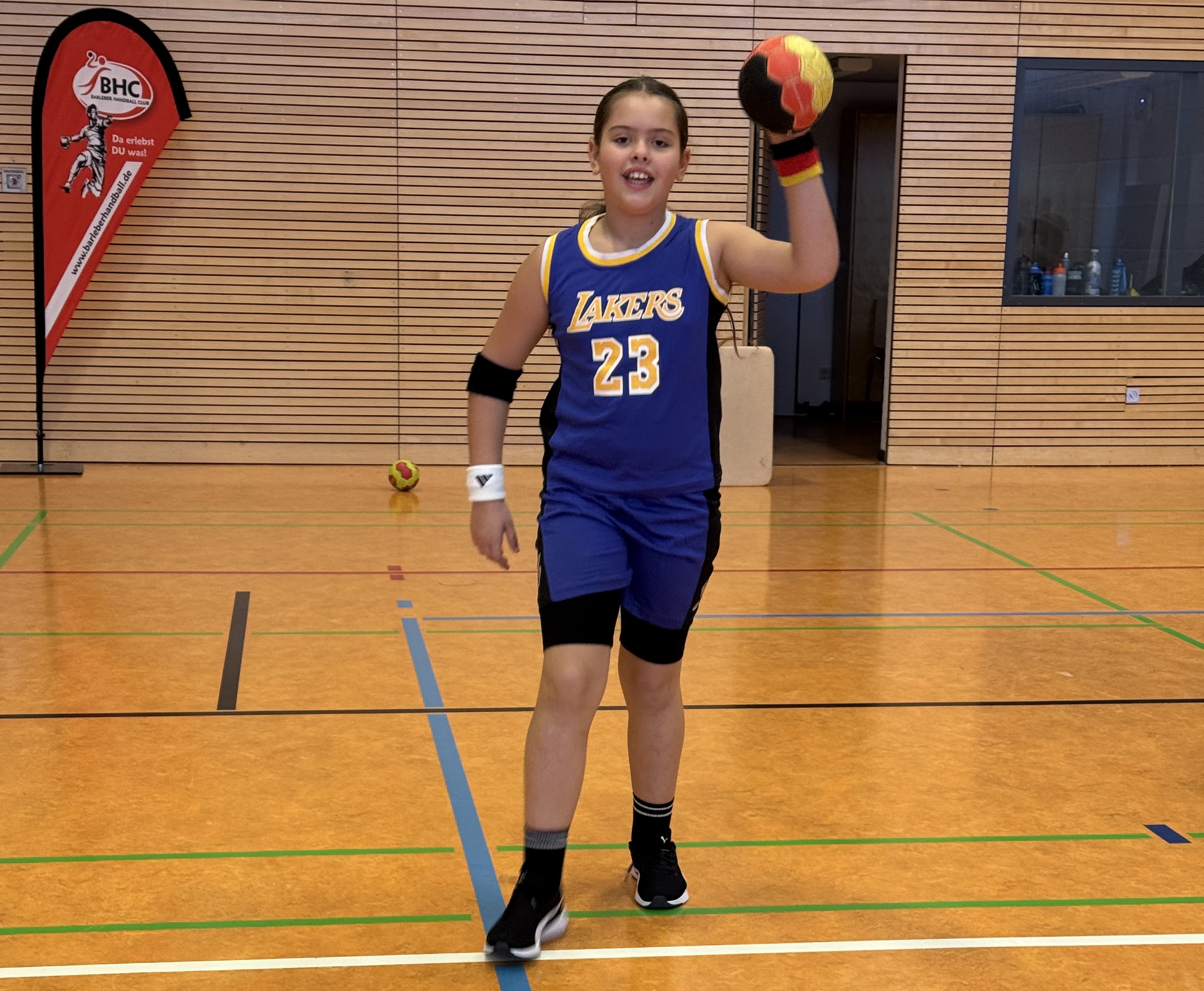 Mädchen im Lakers Basketballtrikot mit Ball in der Hand und freundlichem Gesichtsausdruck