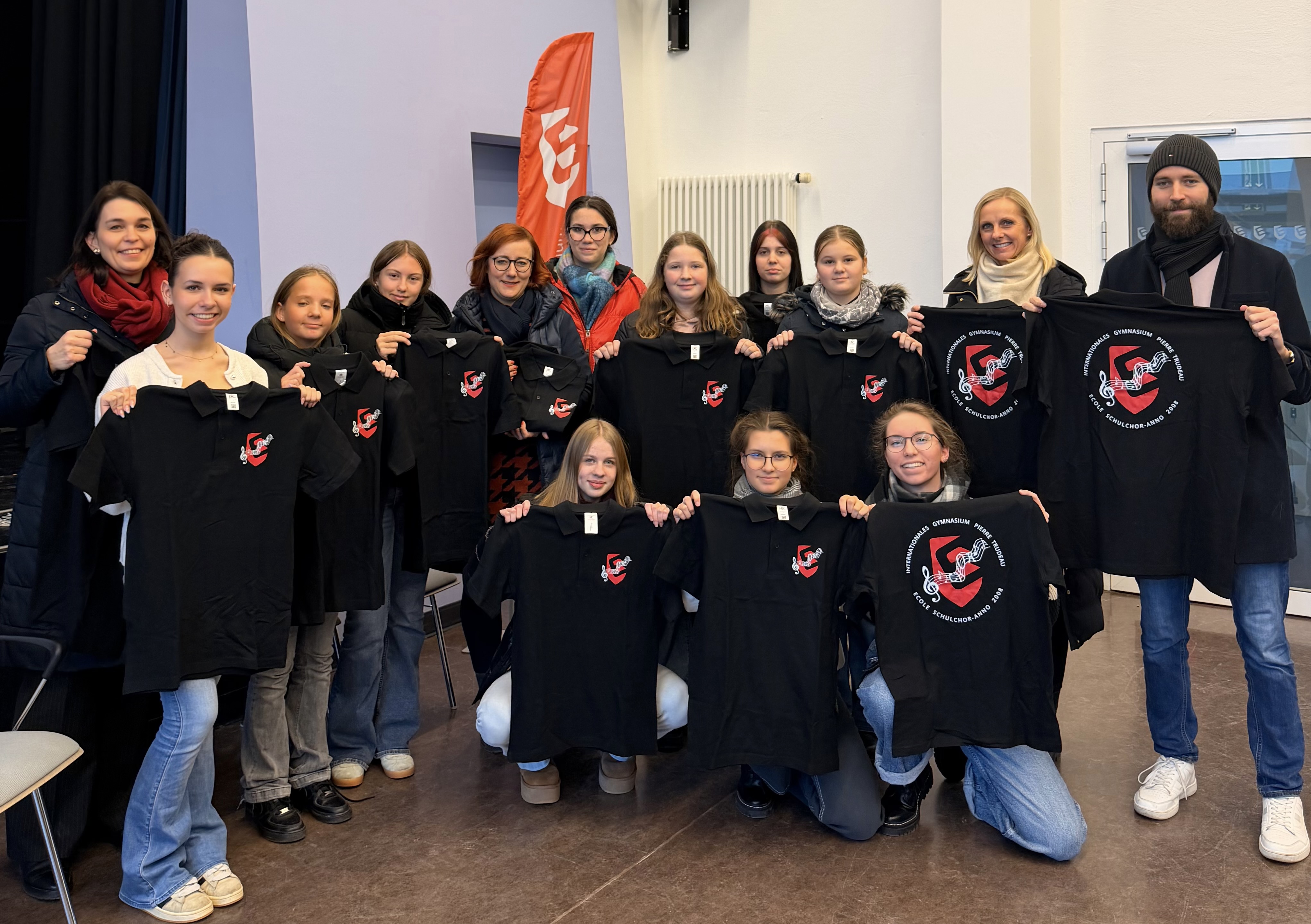 Vierzehn Jugendliche und Erwachsene halten lächelnd schwarze T-Shirts mit rotem Aufdruck